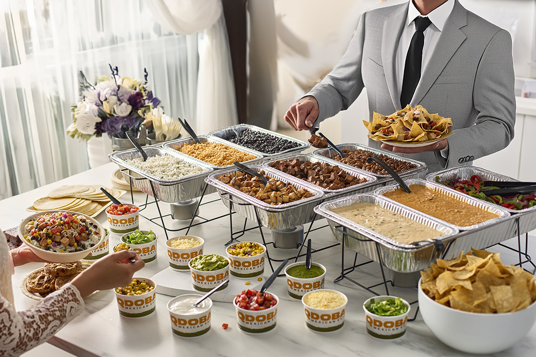 Formal event with a QDOBA catering hot bar featuring trays of rice, beans, meats, queso, chips, and various toppings, highlighting the convenience and hassle-free setup of QDOBA Catering for weddings and related events.