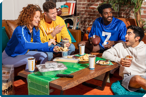 Excited friends sharing easy football party food from QDOBA Mexican Eats, with colorful football jerseys and a festive atmosphere, embodying fun football party ideas and snacks.
