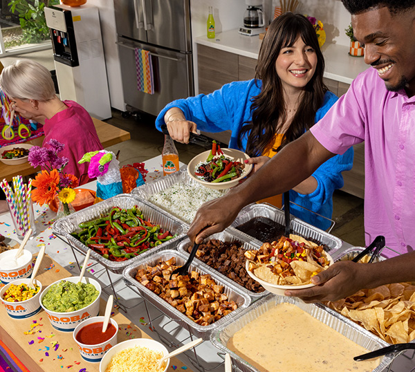 People enjoying a QDOBA Catering hot bar featuring a variety of proteins, vegetables, and toppings, designed to accommodate various dietary needs including vegetarian, vegan, keto, gluten-free, dairy-free, and allergen-safe options.