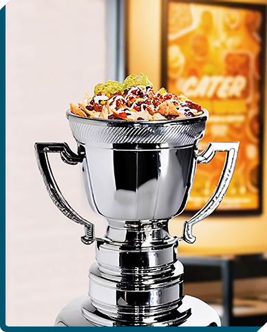 A gleaming trophy brimming with QDOBA's delectable catering selections, crowned with zesty guacamole and sprinkled with savory toppings, celebrating a watch party victory with championship-worthy flavors.