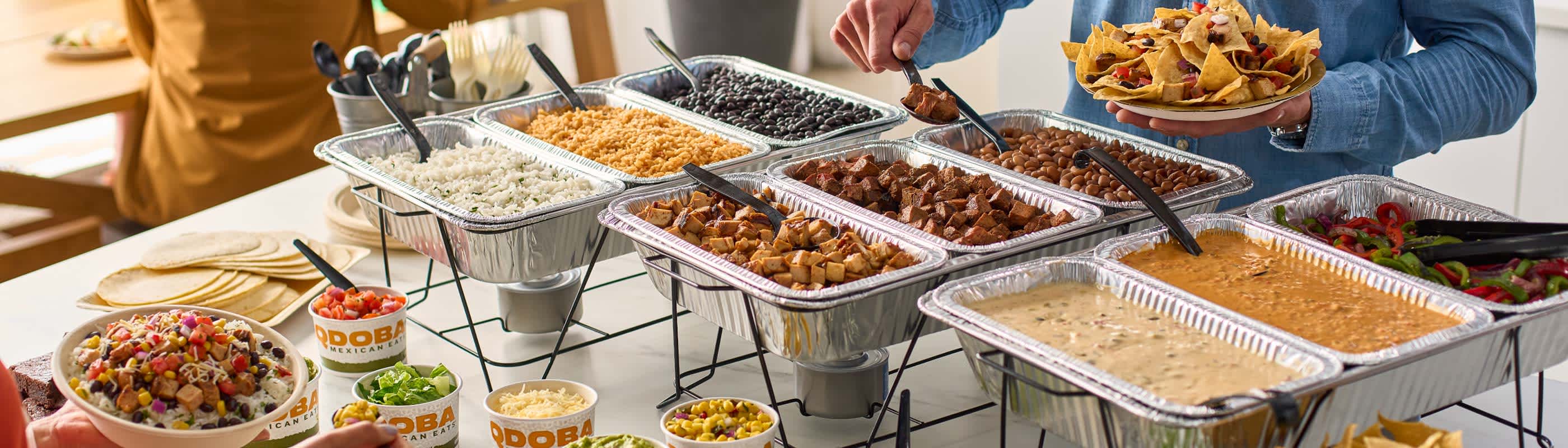 Guests serving themselves at a QDOBA Catering Hot Bar set up onsite.