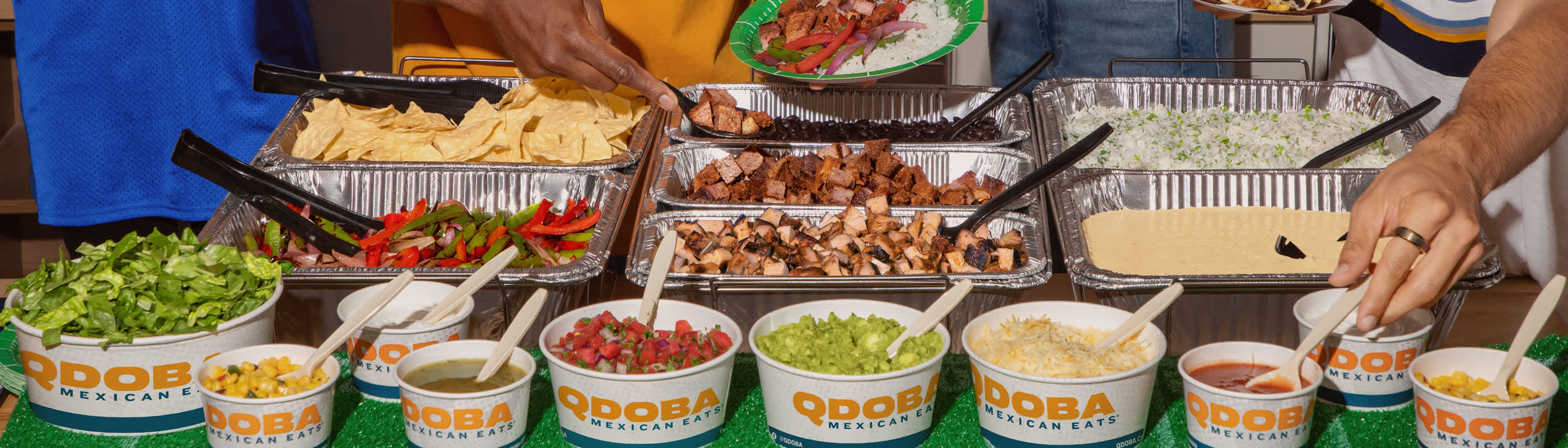 QDOBA Catering spread featuring grilled adobo chicken, tender steak, creamy 3-cheese queso, fresh hand-crafted guacamole, fajita veggies, vibrant pico de gallo, assorted salsas, and a variety of other fresh toppings ready for a festive game day party.