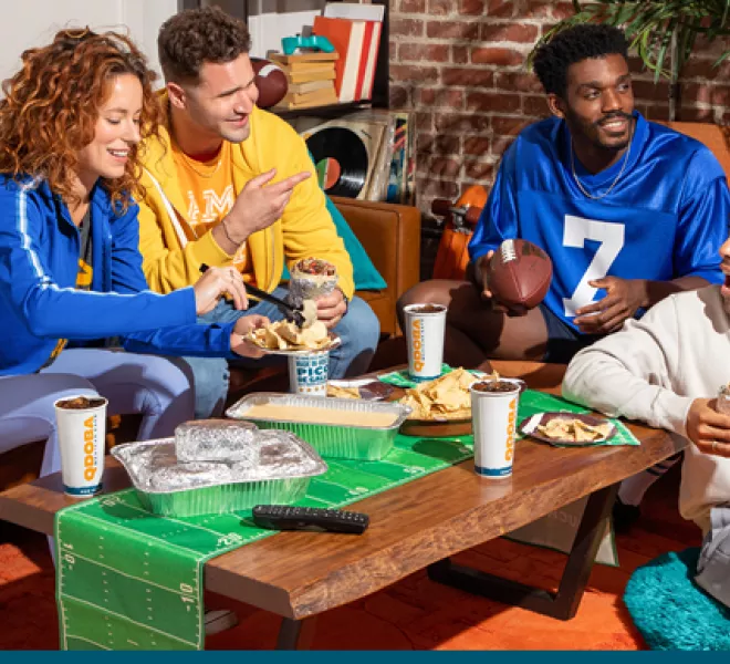 Excited friends sharing easy football party food from QDOBA Mexican Eats, with colorful football jerseys and a festive atmosphere, embodying fun football party ideas and snacks.